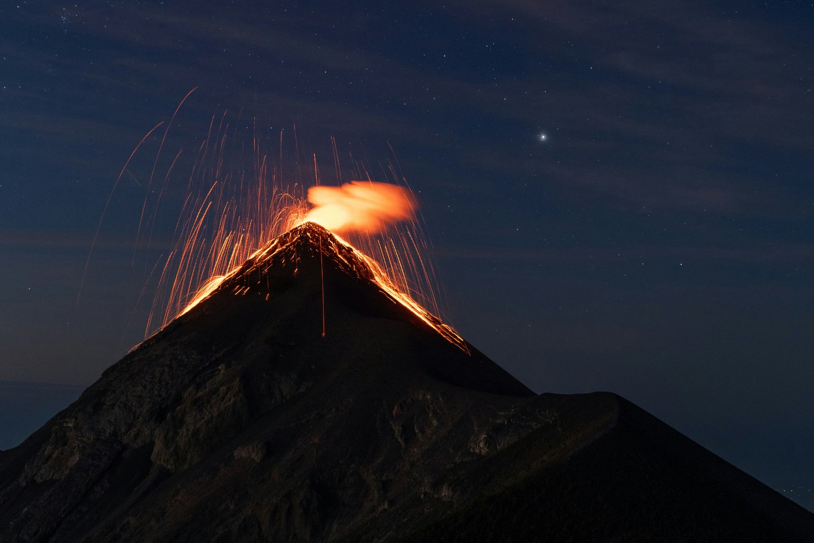 Volcan de Fuego erupting at night with lava fountaining and incandescent ash cloud above the crater against a starry sky
