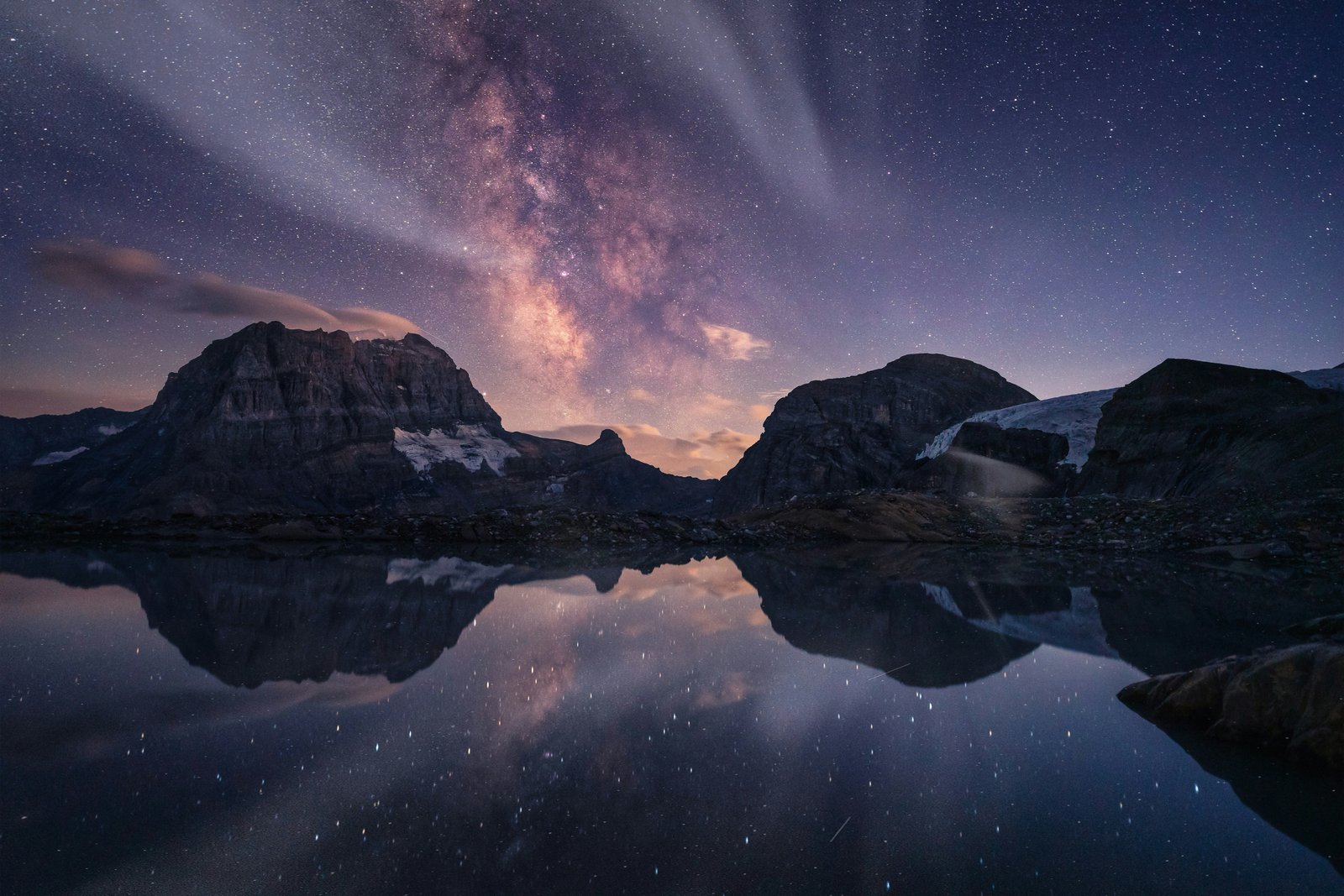 Milky Way reflected in a high mountain lake surrounded by peaks