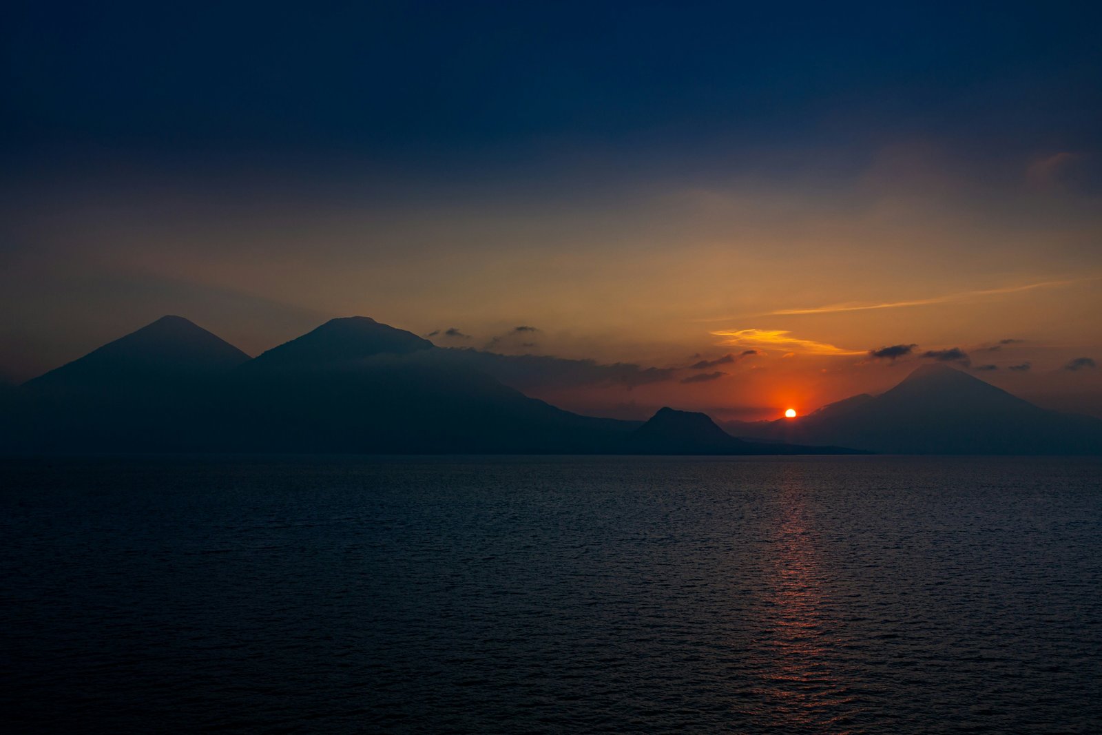 Sunset over Lake Atitlan, four volcano silhouettes against an orange sky