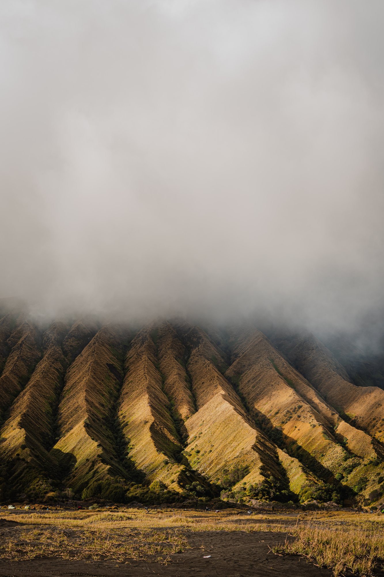 The same wall in the fog, its top dissolved. The savannah at its foot is the only flat ground in sight.
