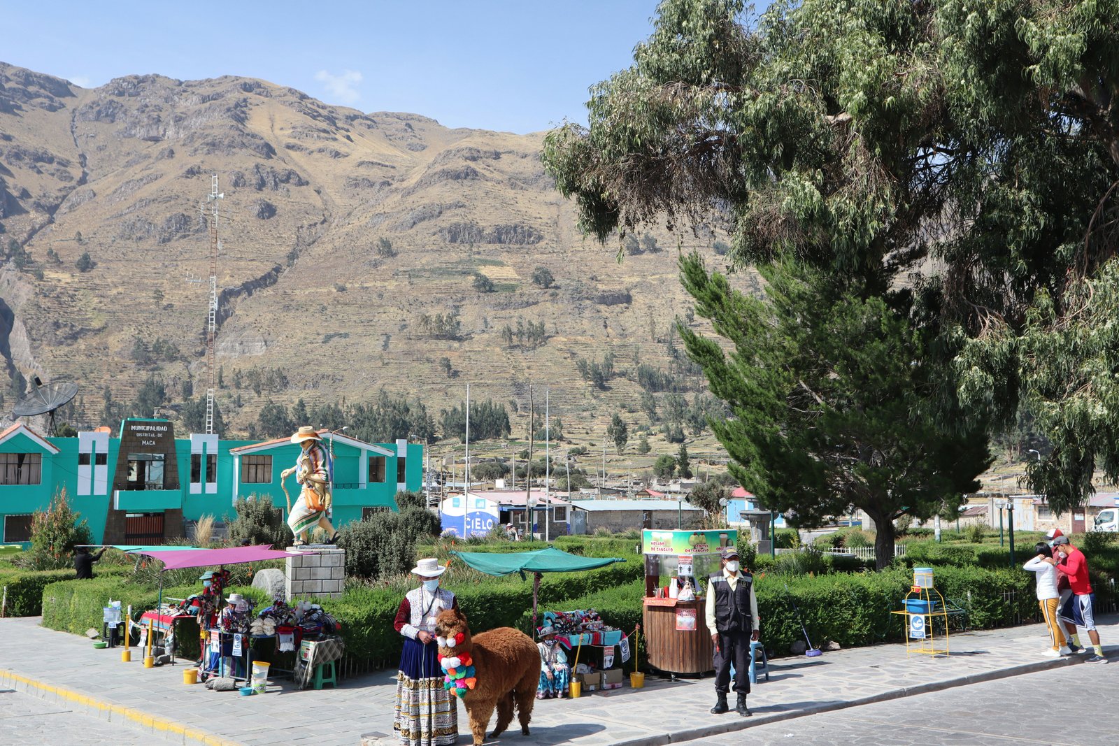Plaza de Maca village in the canyon, woman in traditional dress with an alpaca in front of colonial buildings