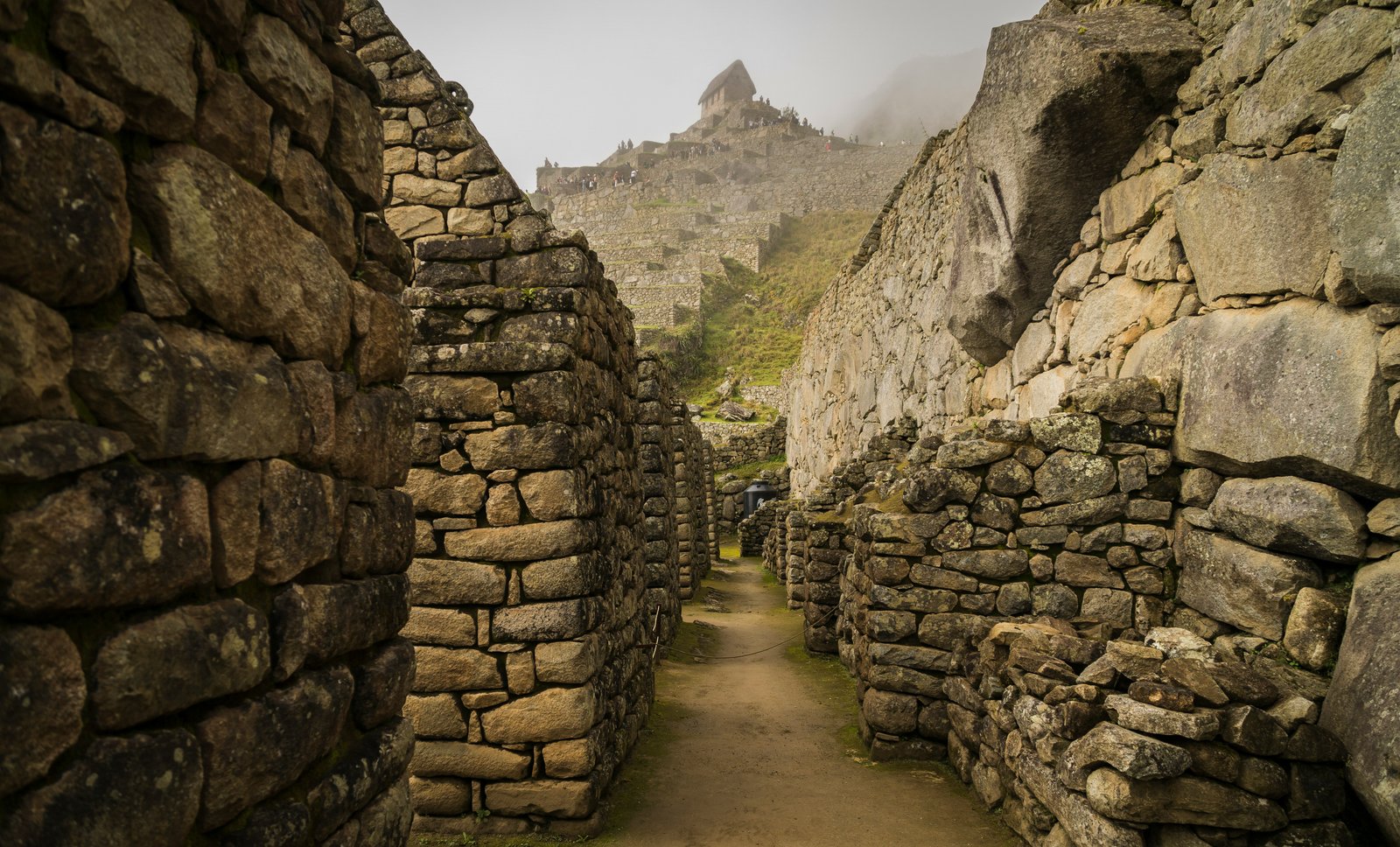 Narrow stone corridor between Inca walls leading toward the Machu Picchu citadel in morning mist