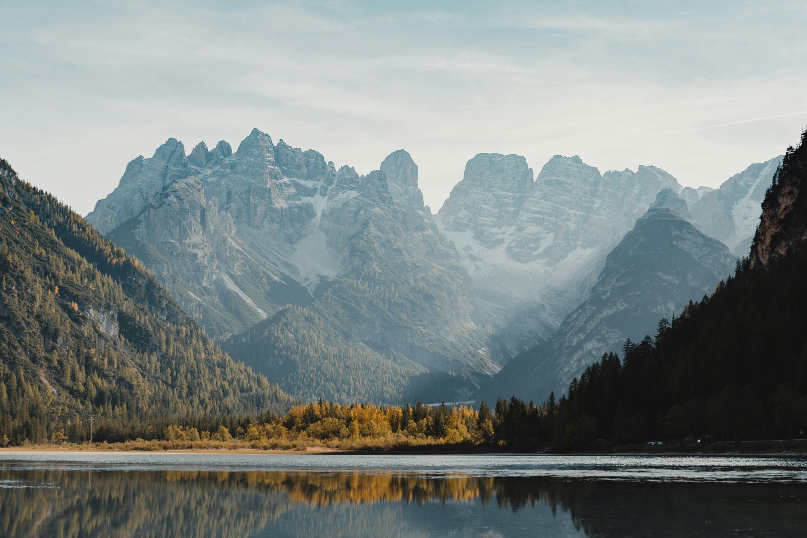 Autumn larch forest reflected in an alpine lake below the Cristallo massif