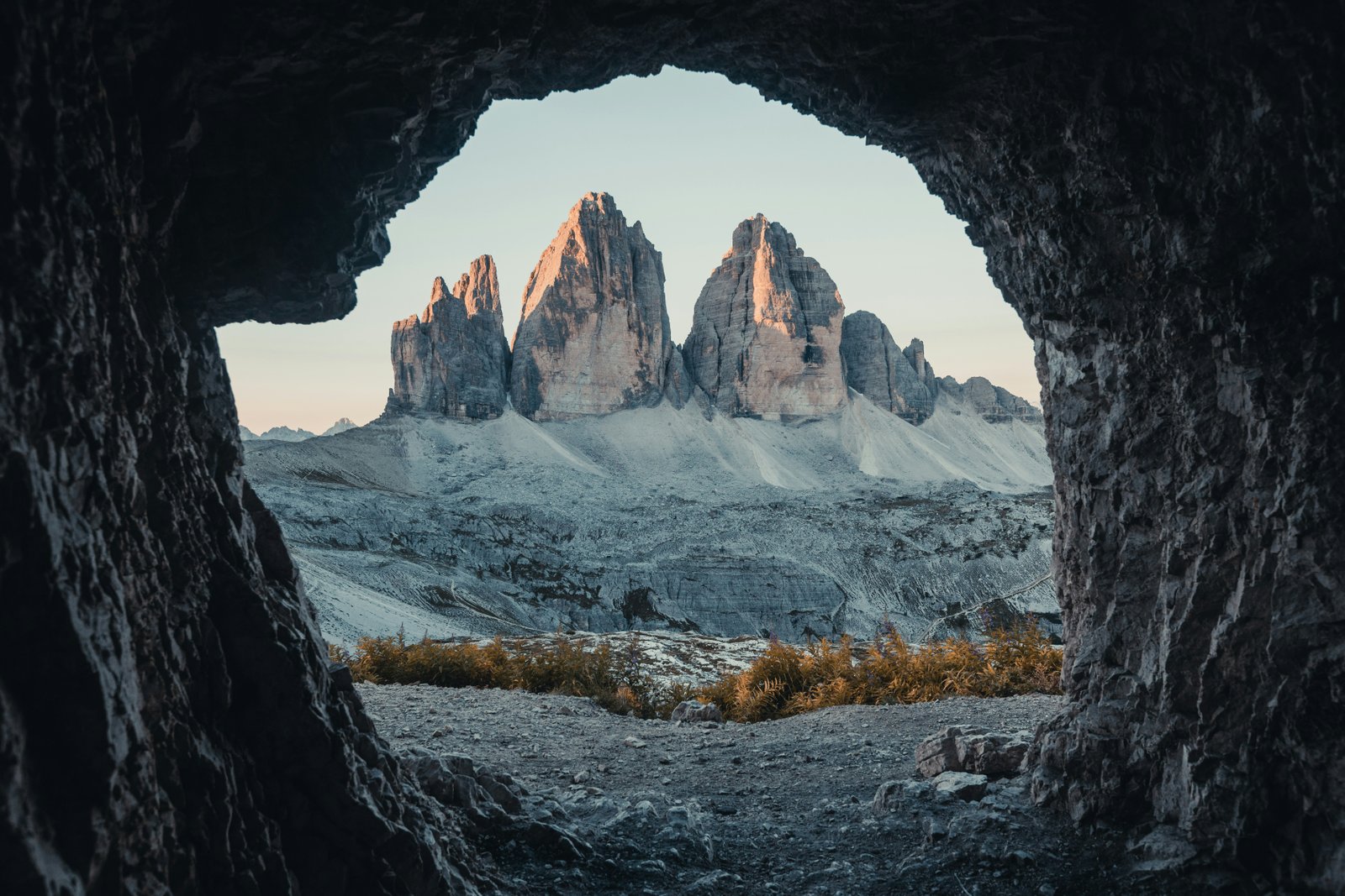 Tre Cime di Lavaredo framed through a rock arch at alpenglow