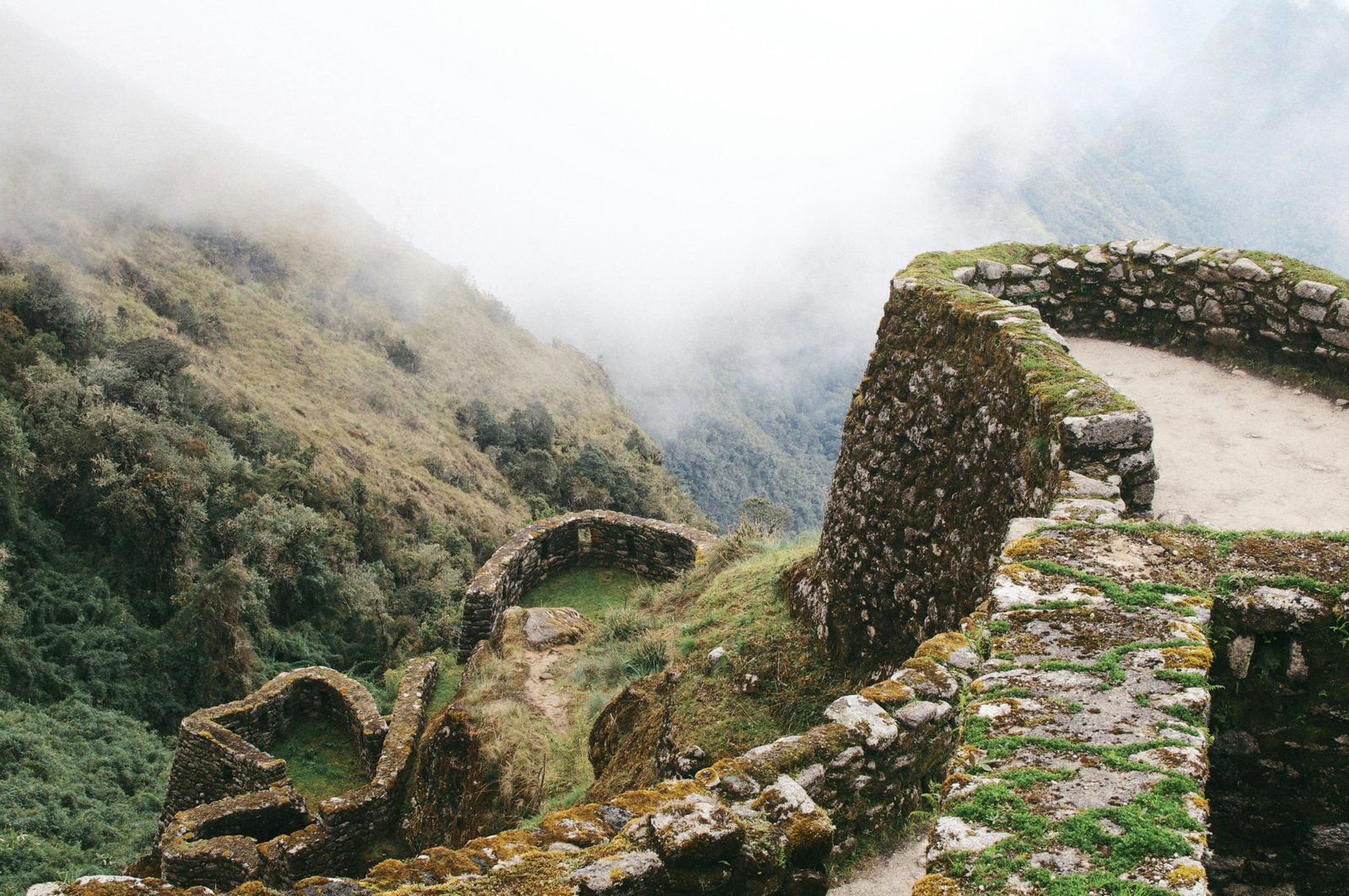 Inca stone arches and walls at a trail ruin, cloud forest and mist rising behind