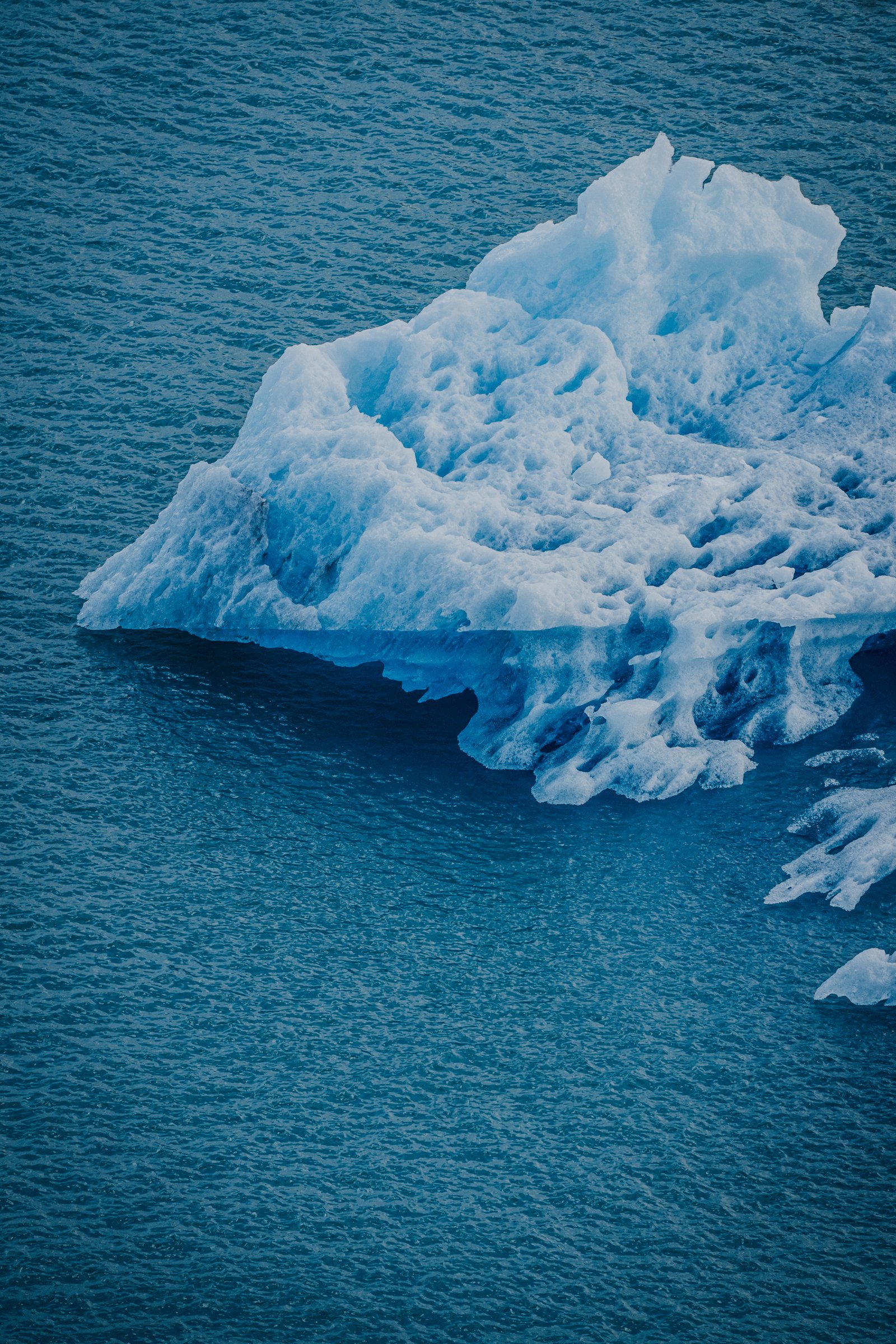Single iceberg adrift in deep blue lake water.