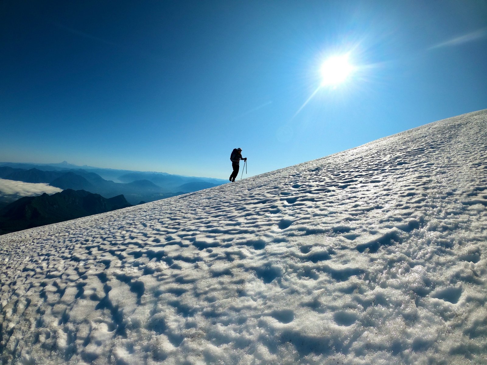 Climber ascending the snowfield near the crater rim, lakes and clouds far below
