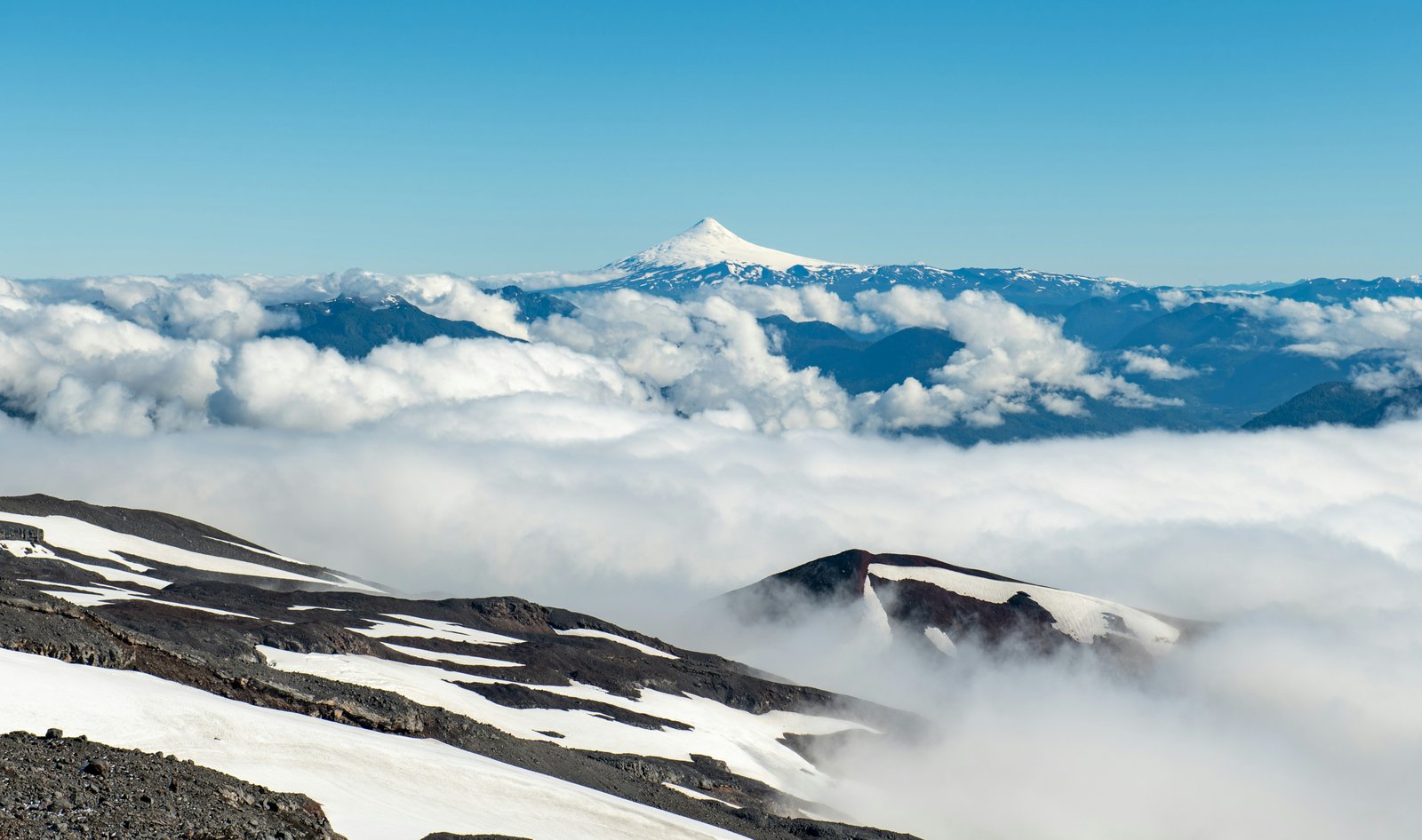 View from near the Villarrica crater looking toward a snow-capped volcano above a sea of clouds