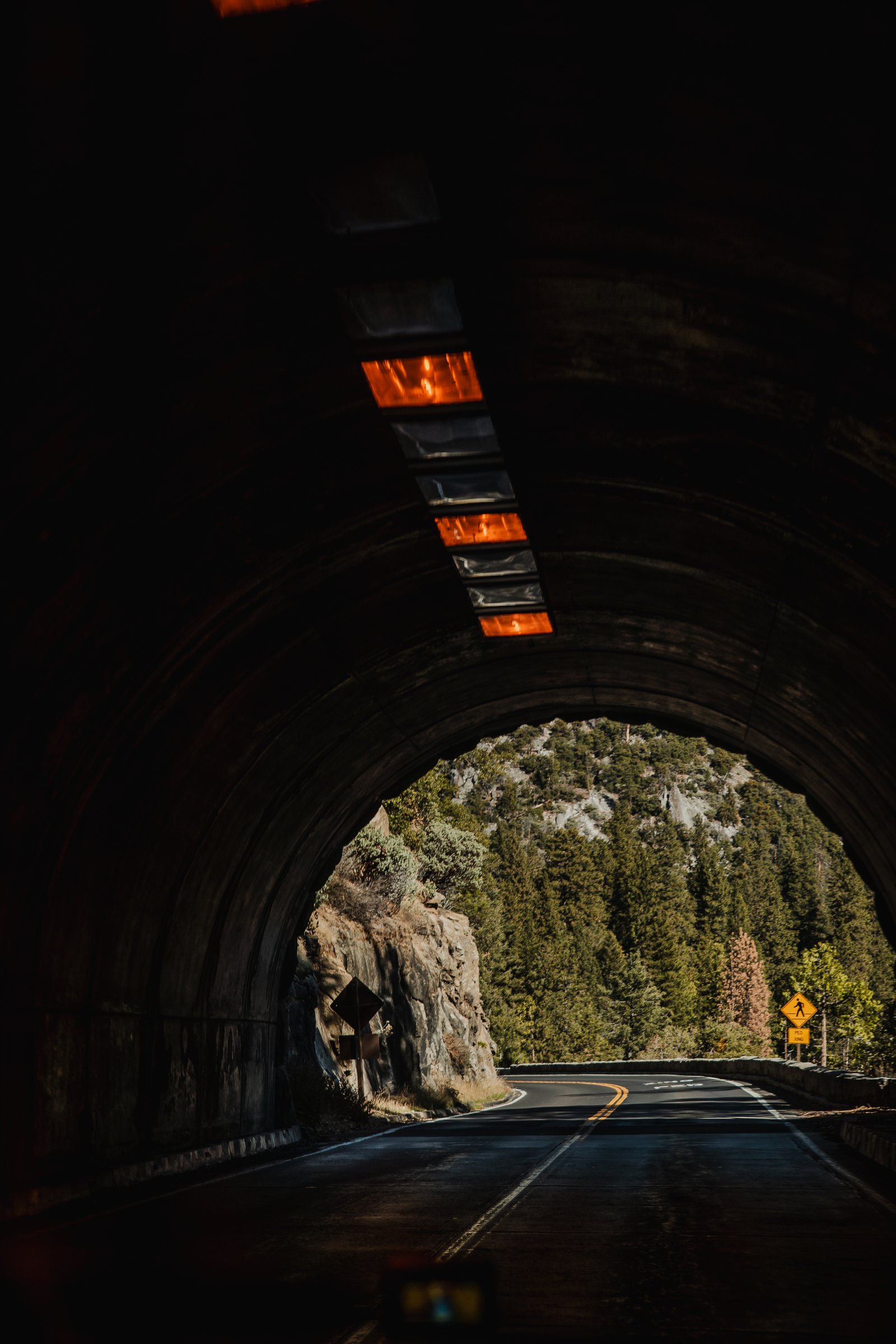 Inside the Wawona Tunnel. Orange lamps illuminate the vault above the empty road.