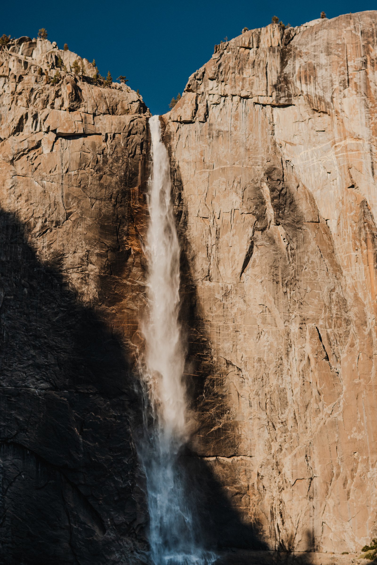 Upper Yosemite Falls on warm granite. The fall cuts between two walls of orange stone.